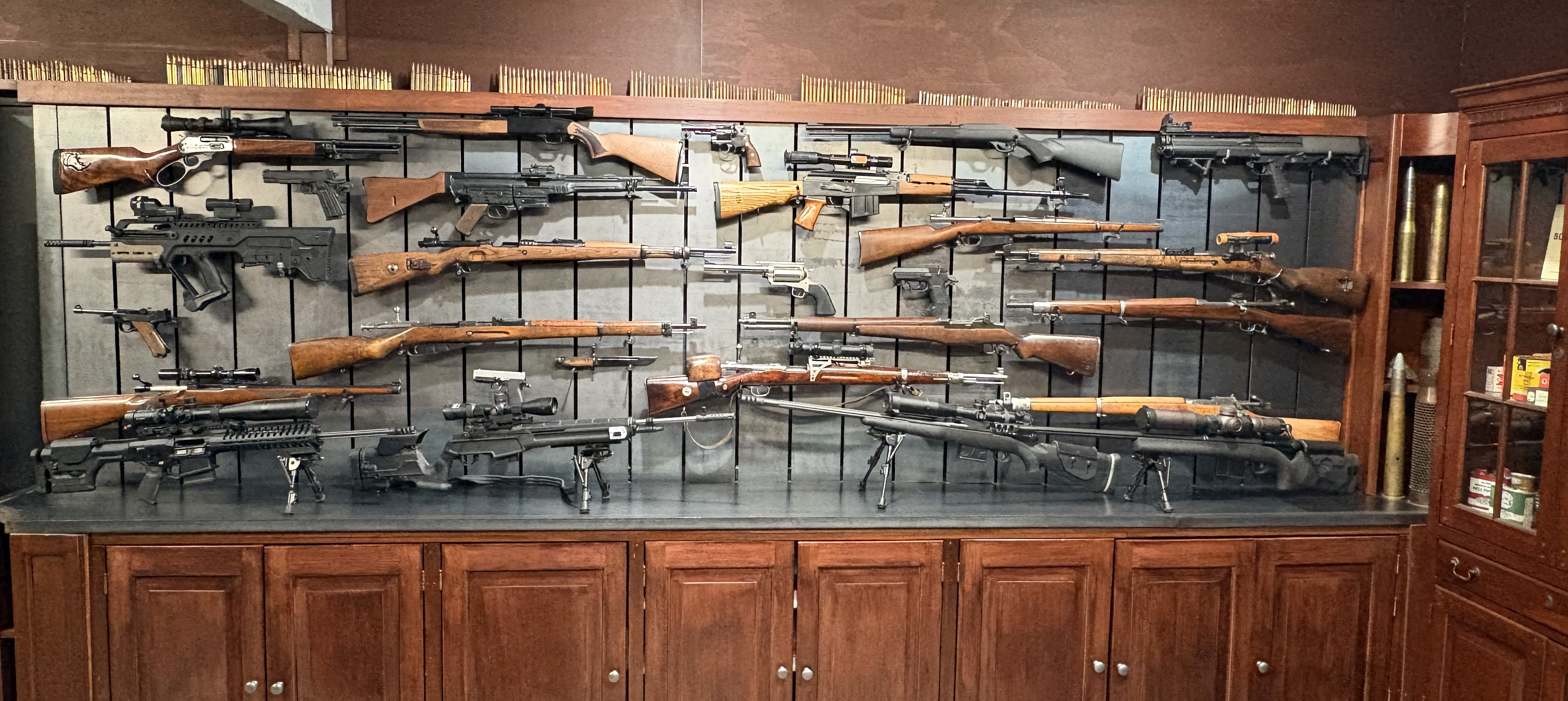 A long steel display wall holding rifles and pistols that appear to float in front of it