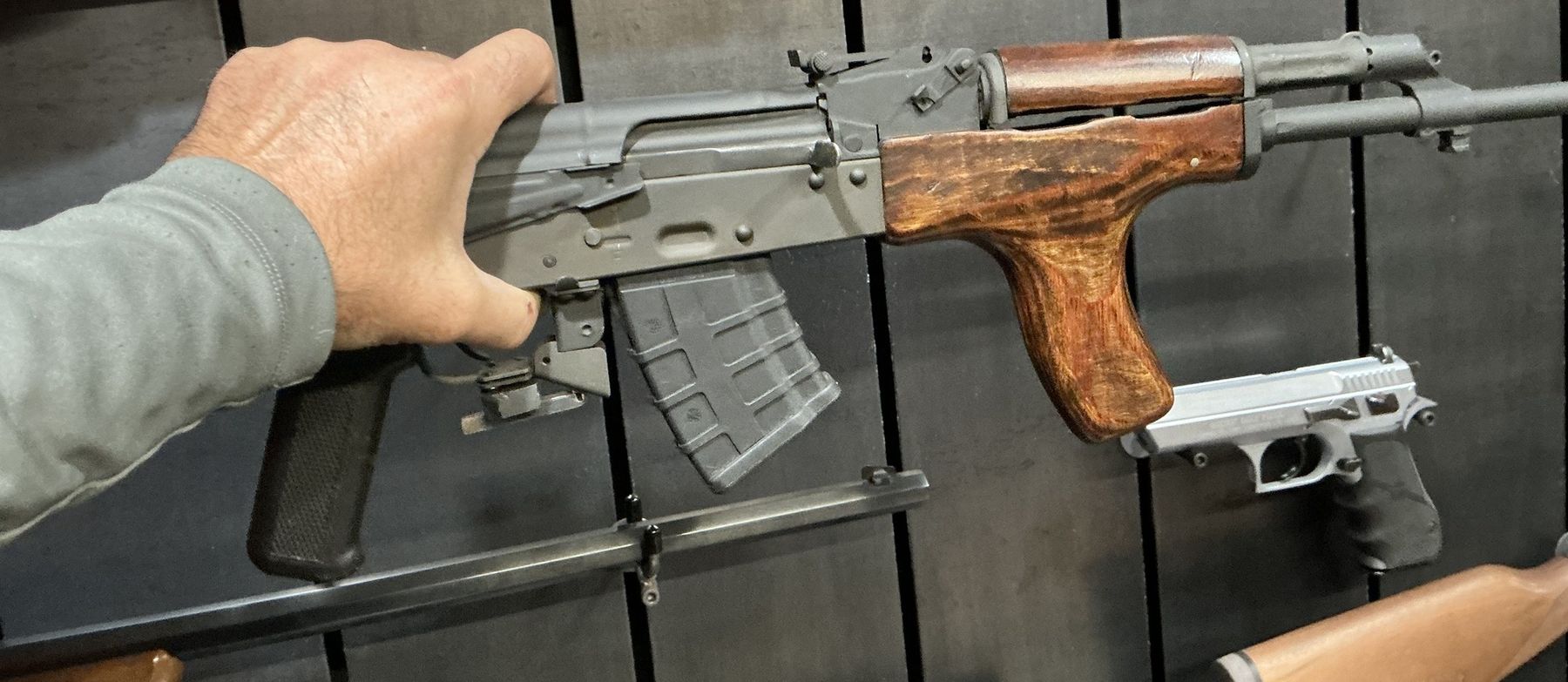 A hand lifting a rifle off the steel wall