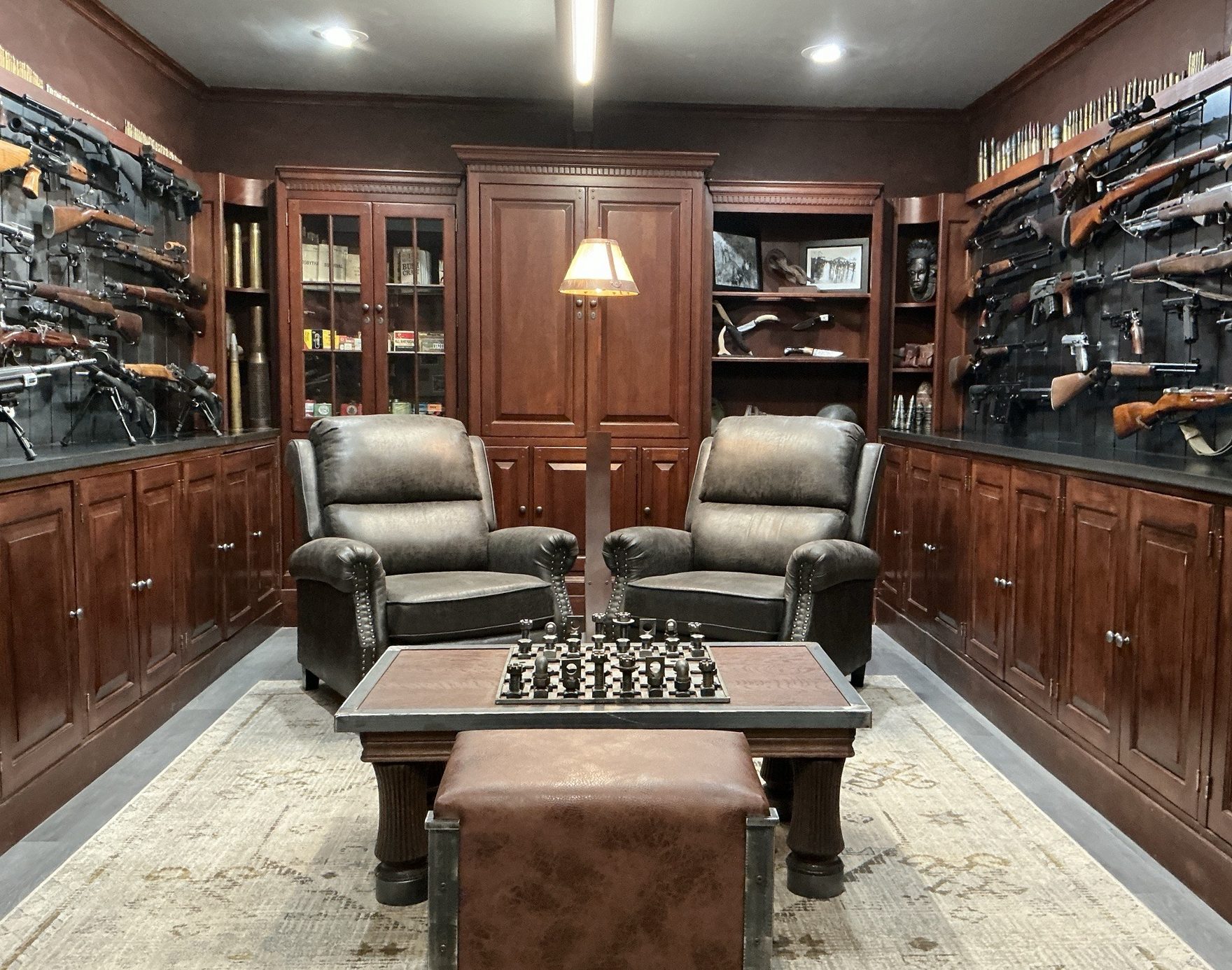 A finished gun room with two leather chairs, a lamp, a chess table and steel walls on both sides